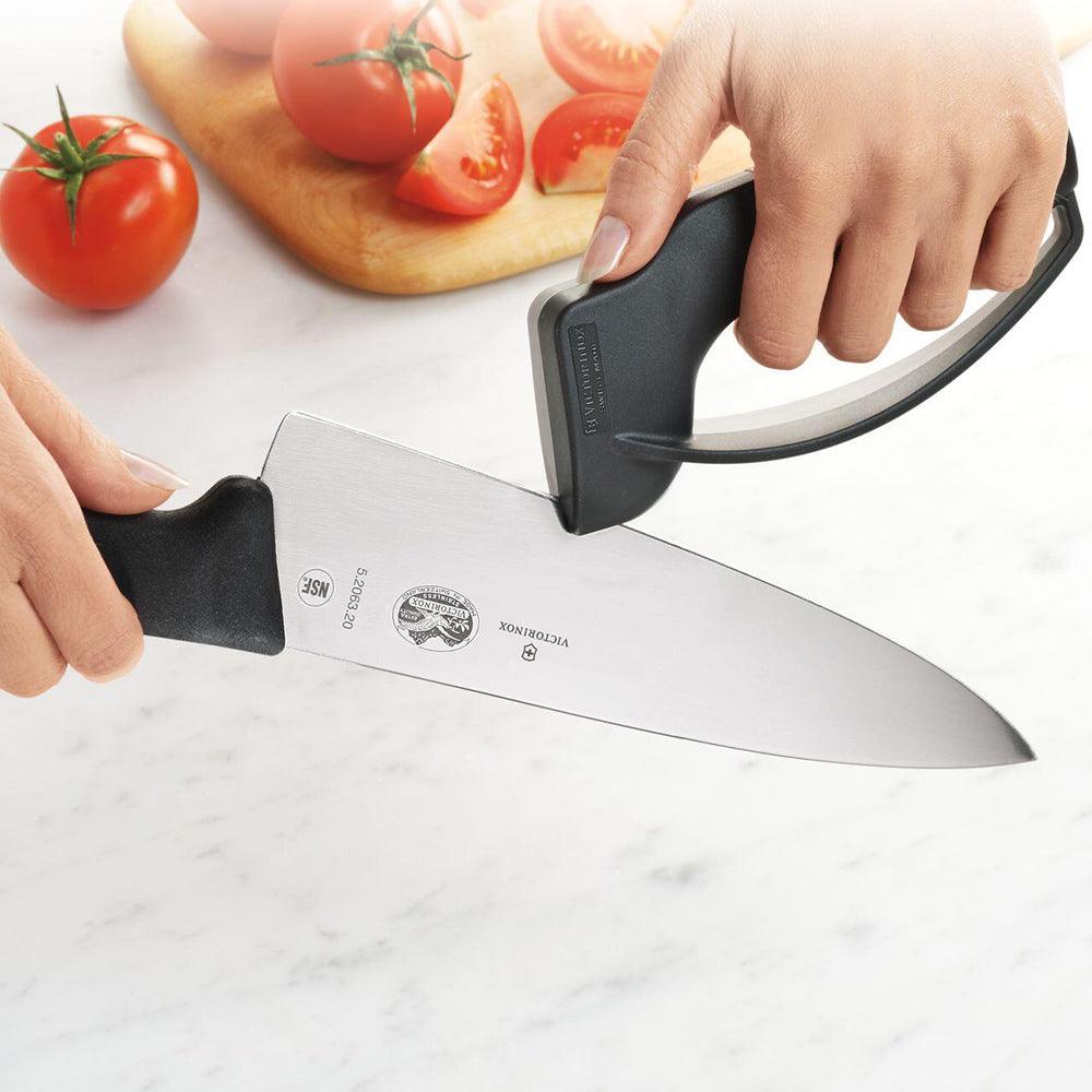 Victorinox Knife Sharpener - black V-shaped carbide sharpener with guard being drawn along a stainless steel knife blade